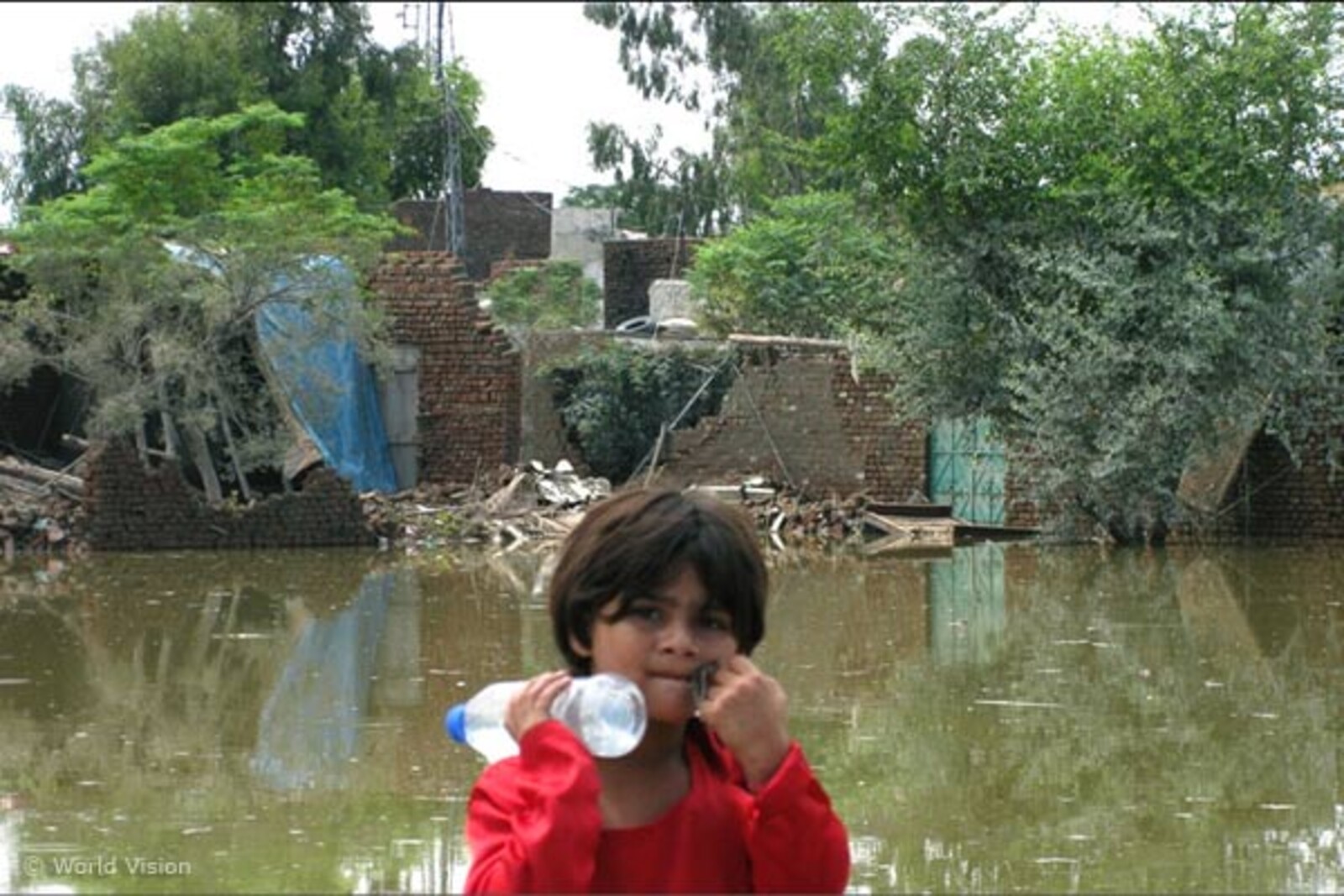 Flut Pakistan: Mädchen mit Wasserflasche vor überschwemmtem Gebiet