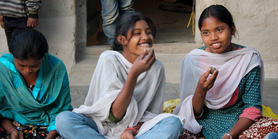 Mädchen essen vor einem Schulgebäude in Indien