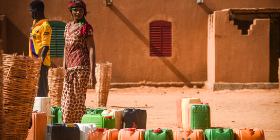 Ein Mann und eine Frau stehen im Niger neben Kanistern für Wasservorräte