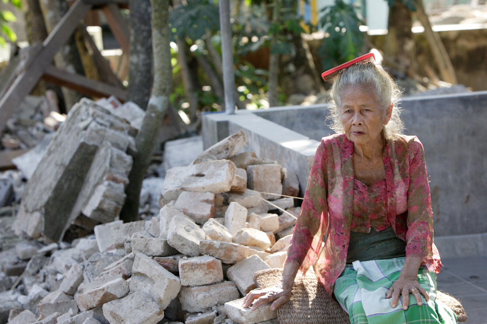 Eine alte Dame sitzt in den Trümmern, die einst ihr Haus waren. Gerade ältere Menschen haben große Nachteile bei einer Katastrophe, denn sie haben kein Einkommen und sind oft körperlich beeinträchtigt.