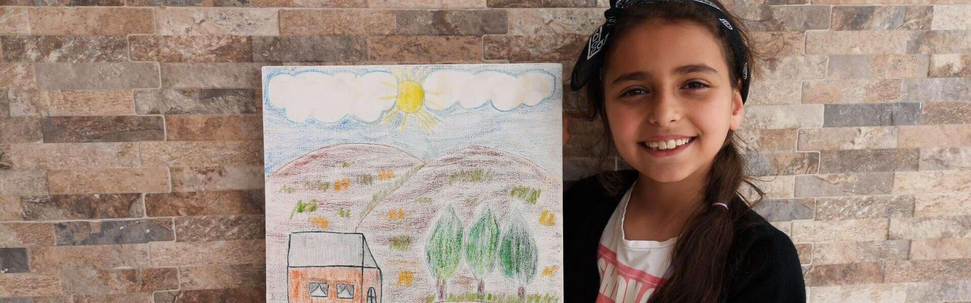 Ein Mädchen aus Syrien hält ein selbstgemaltes Bild in die Kamera