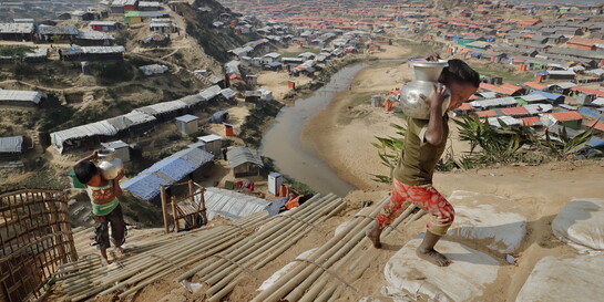 Zwei Kinder in der Flüchtlingssiedlung Cox’s Bazar in Bangladesch tragen gusseiserne Wasserkrüge eine provisorische Bambustreppe hinauf