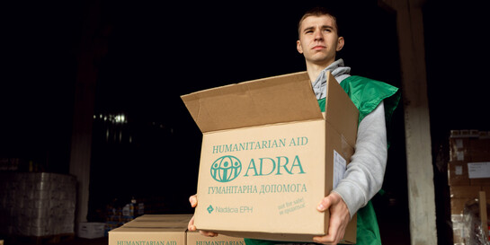 Ein Helfer der Organisation ADRA trägt ein Paket mit Hilfsgütern