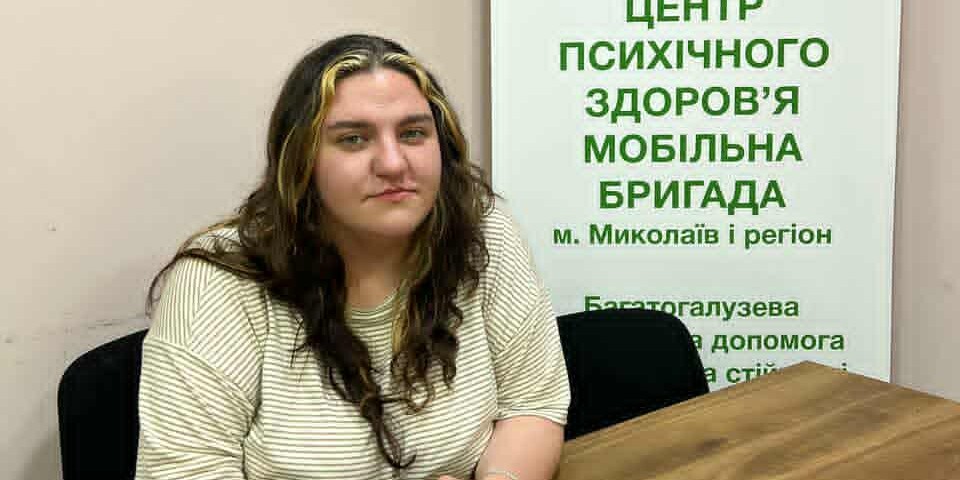 Liza musste selbst aus ihrer Heimat Ukraine fliehen, ist zurückgekehrt und arbeitet heute als Psychologin Junge ukrainische Frau sitzt mit zusammengefalteten Händen an einem Tisch und schaut in die Kamera