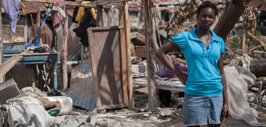 Frau steht vor einer Ruine auf Haiti nach dem Hurrikan Matthew