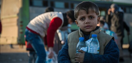 Junge steht mit Wasserfalschen in Aleppo.