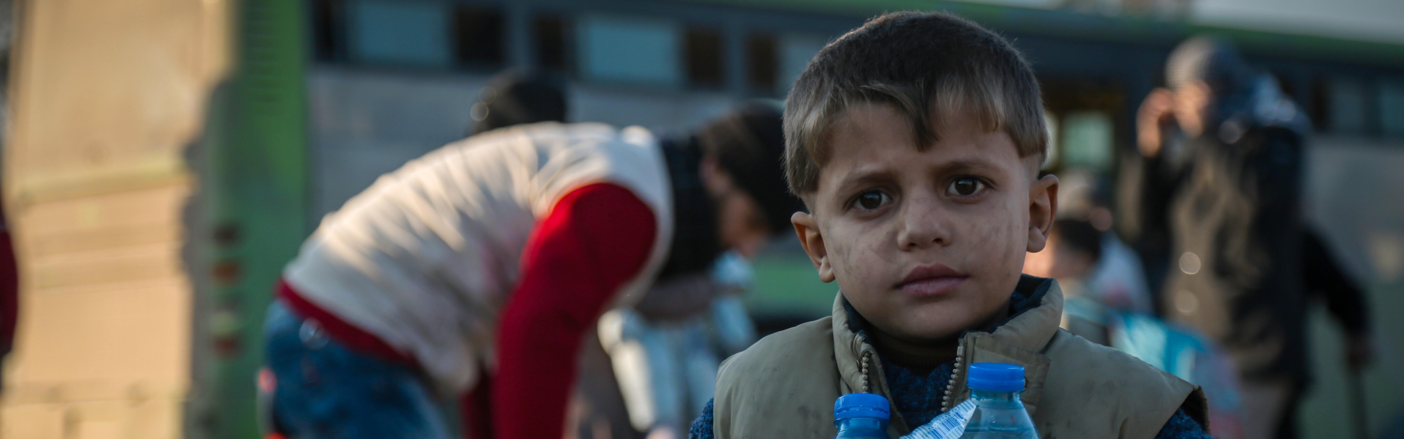 Junge steht mit Wasserfalschen in Aleppo.