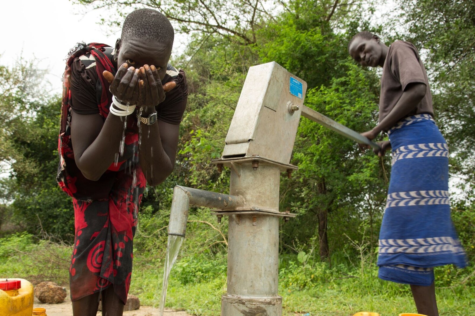 Zwei Männer im Südsudan trinken Wasser aus einer Pumpe.