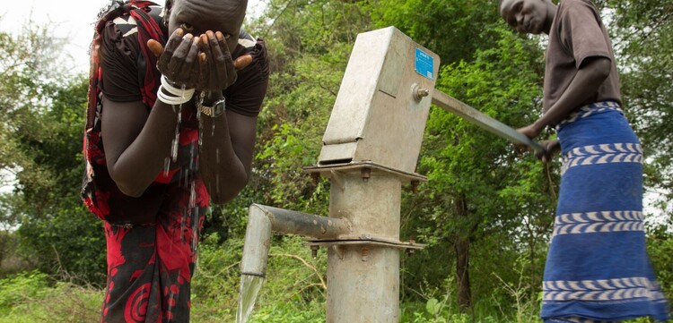 Zwei Männer im Südsudan trinken Wasser aus einer Pumpe