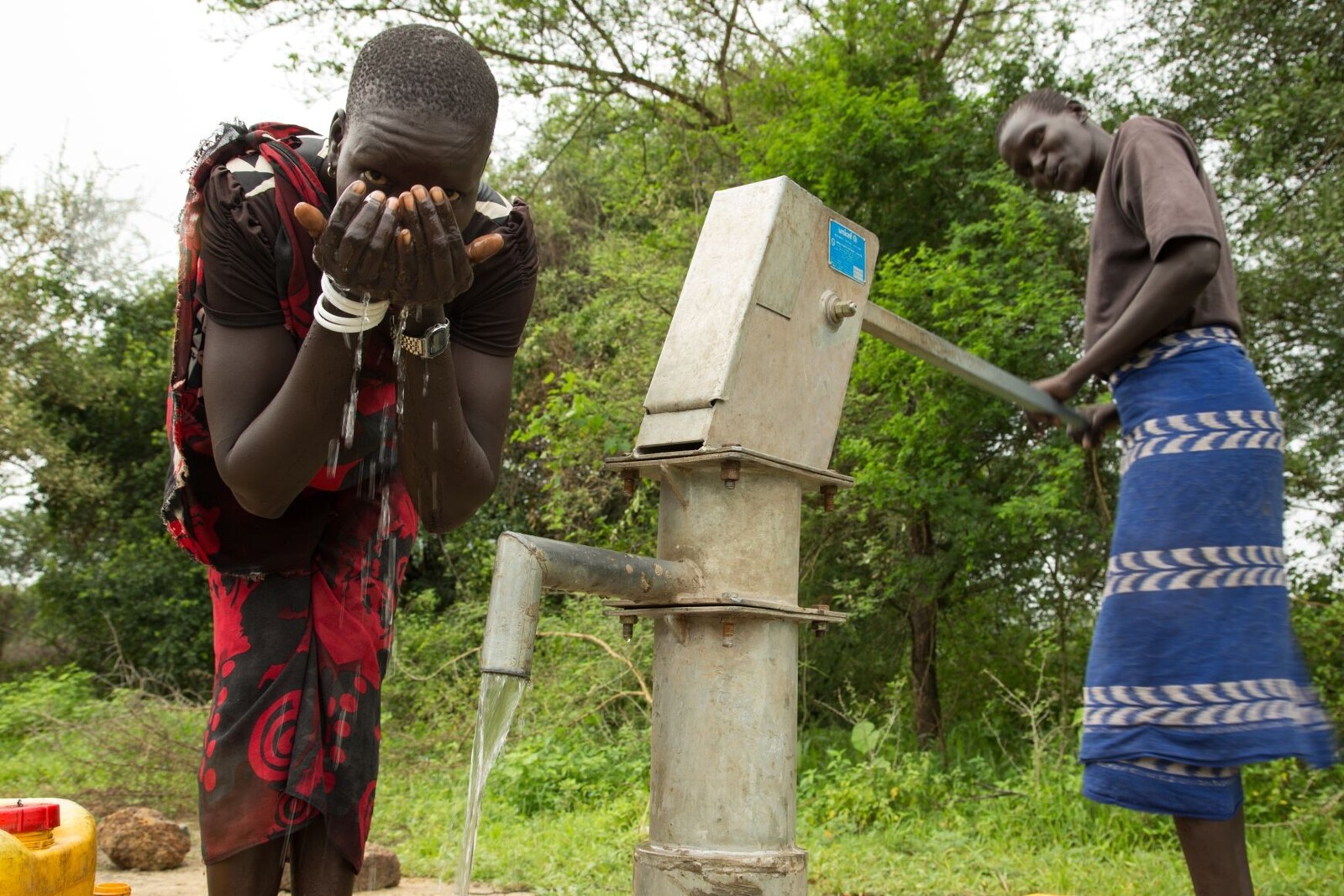 Zwei Männer im Südsudan trinken Wasser aus einer Pumpe