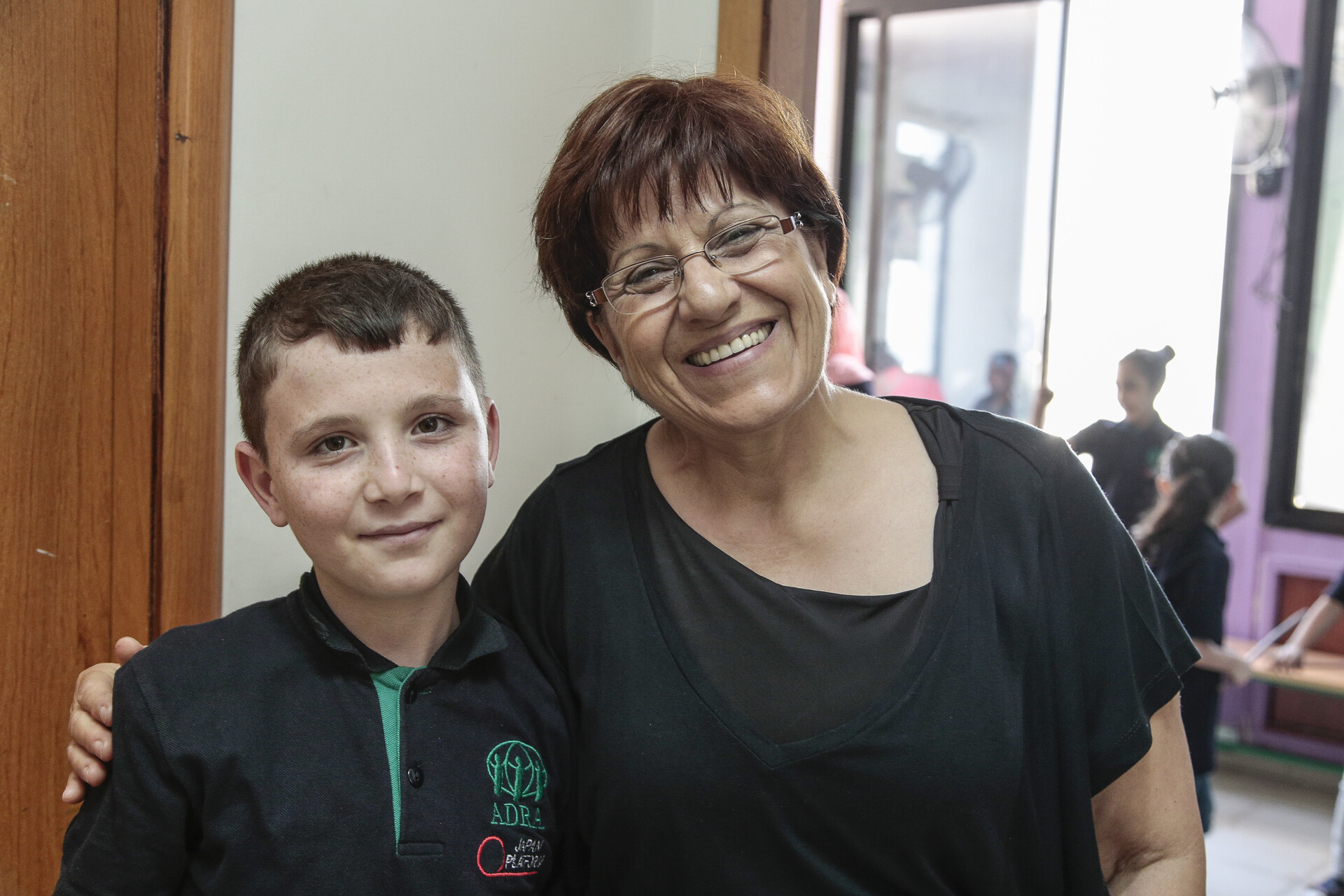 Adnan steht neben einer Lehrerin. Adnan ist ein Flüchtlingskind aus Syrien in einer Schule in Beirut.