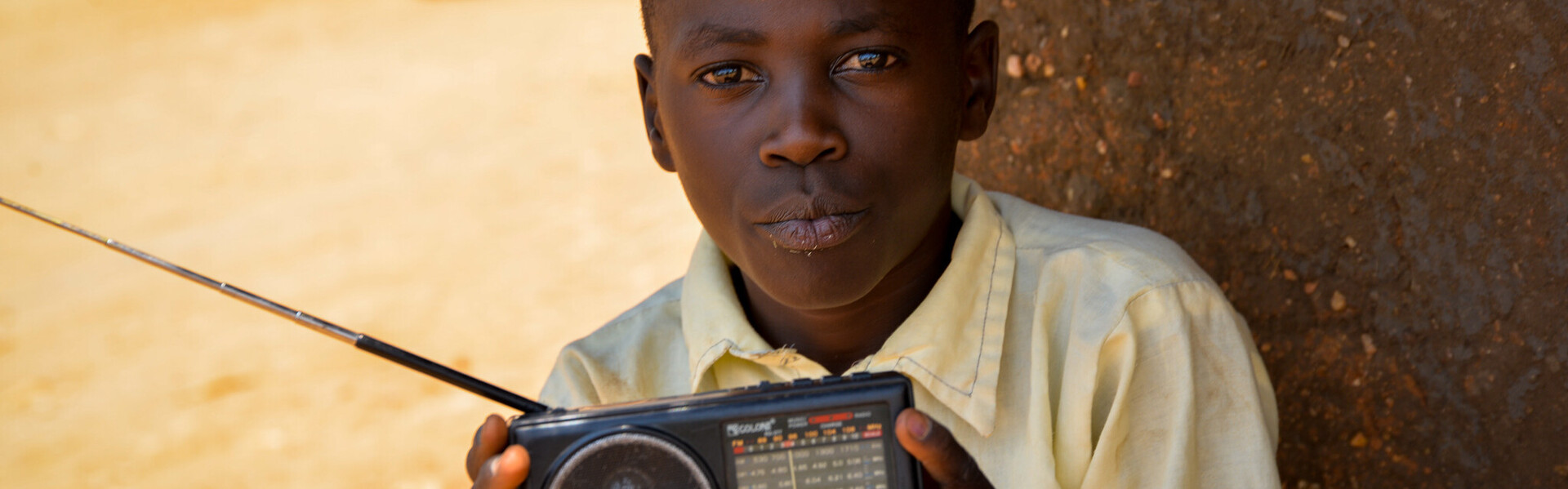 Über ein kleines tragbares Radio empfängt Samuel aus Uganda die neuesten Meldungen zum Coronavirus