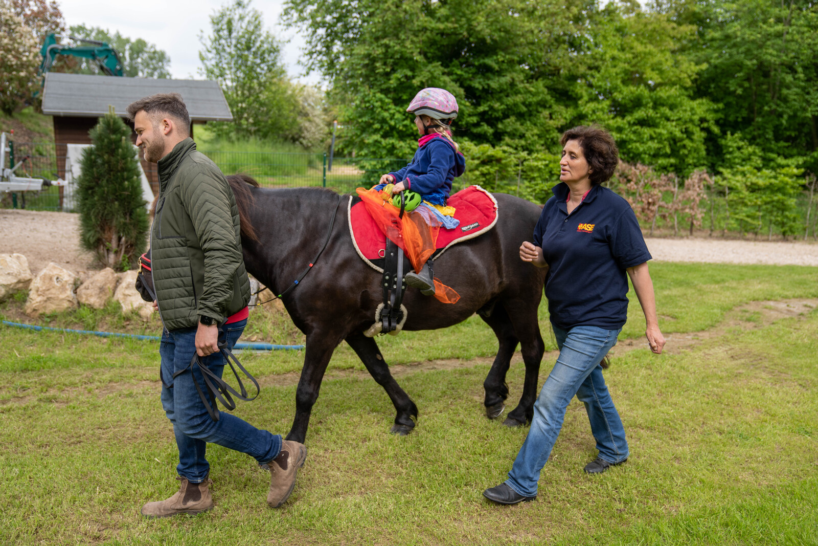 Ein Mann und eine Frau begleiten ein kleines Mädchen auf dem Pferd