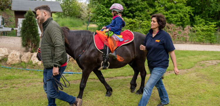 Ein Mann und eine Frau begleiten ein kleines Mädchen auf dem Pferd