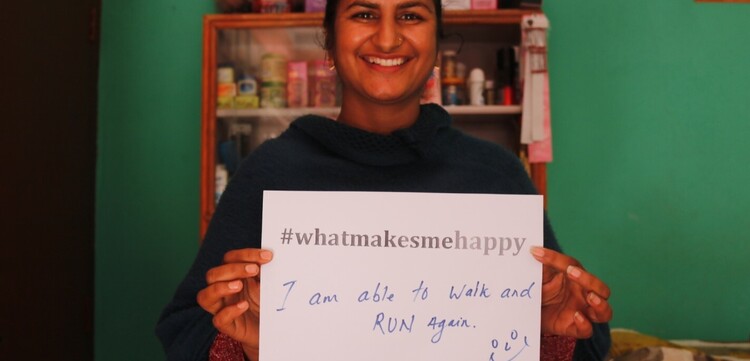 Eine Frau hält einen Zettel in Nepal in der Hand mit der Aufschrift "#whatmakesmehappy". Sie freut es, dass Sie wieder laufen kann