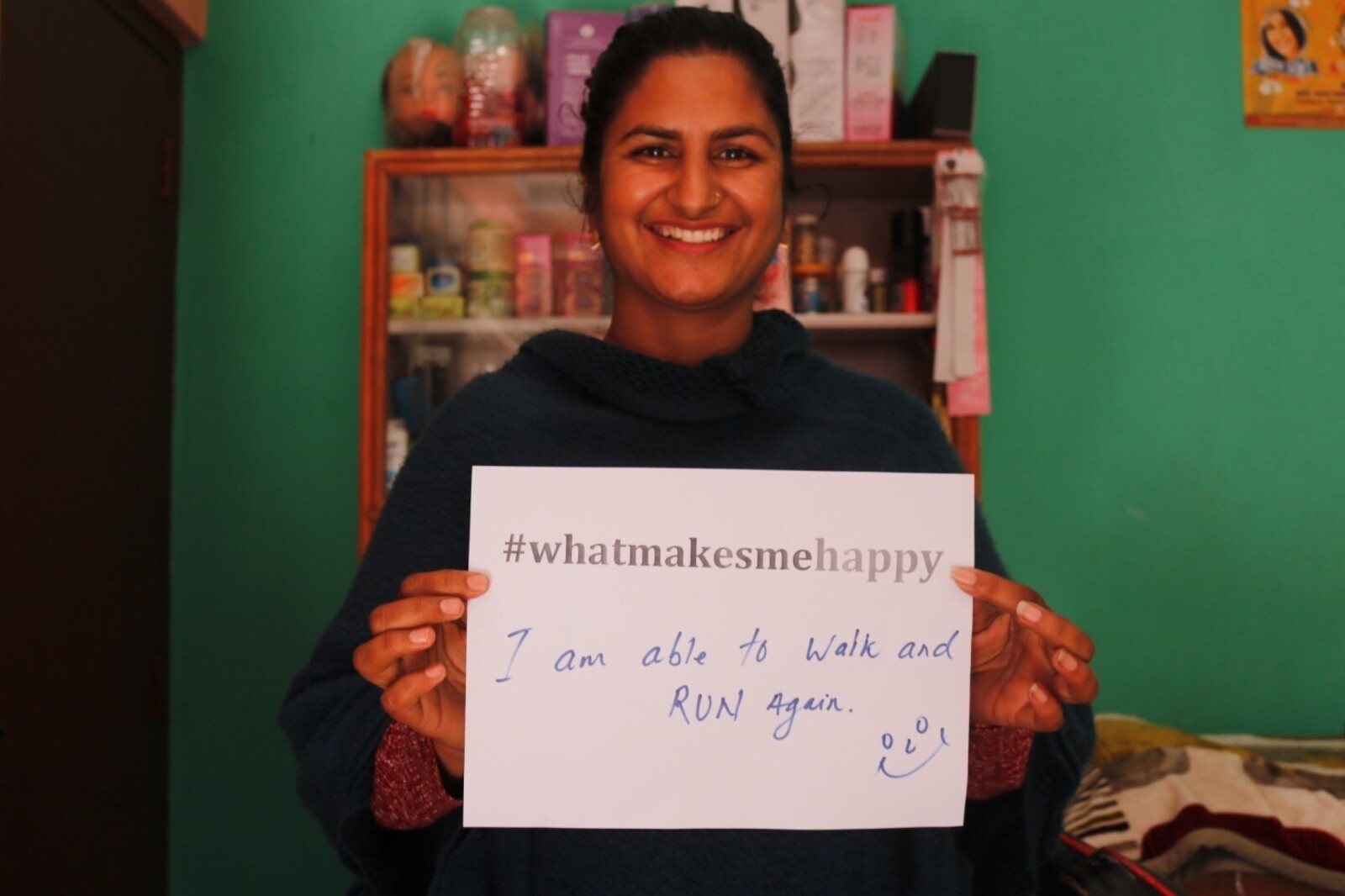 Eine Frau hält einen Zettel in Nepal in der Hand mit der Aufschrift "#whatmakesmehappy". Sie freut es, dass Sie wieder laufen kann