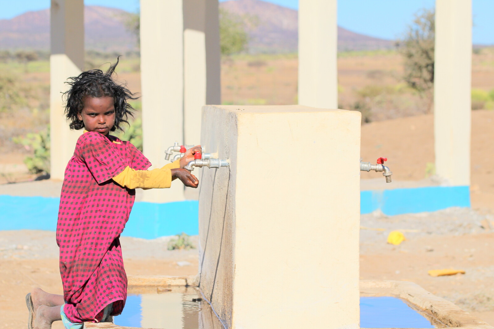 Ein Mädchen hält in Somalia die Hände unter das Wasser, das aus einer neuen Pumpe läuft.