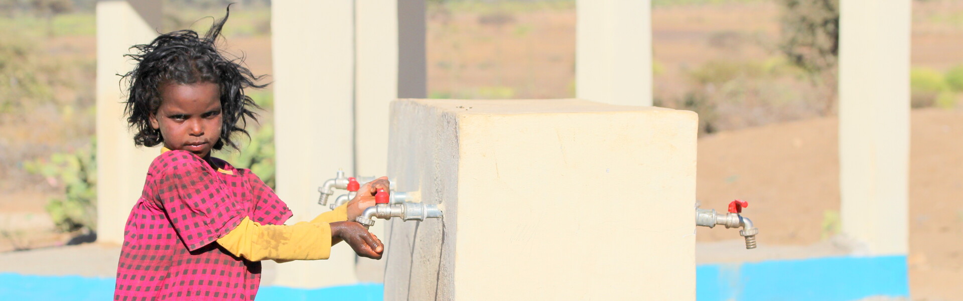 Ein Mädchen hält in Somalia die Hände unter das Wasser, das aus einer neuen Pumpe läuft.