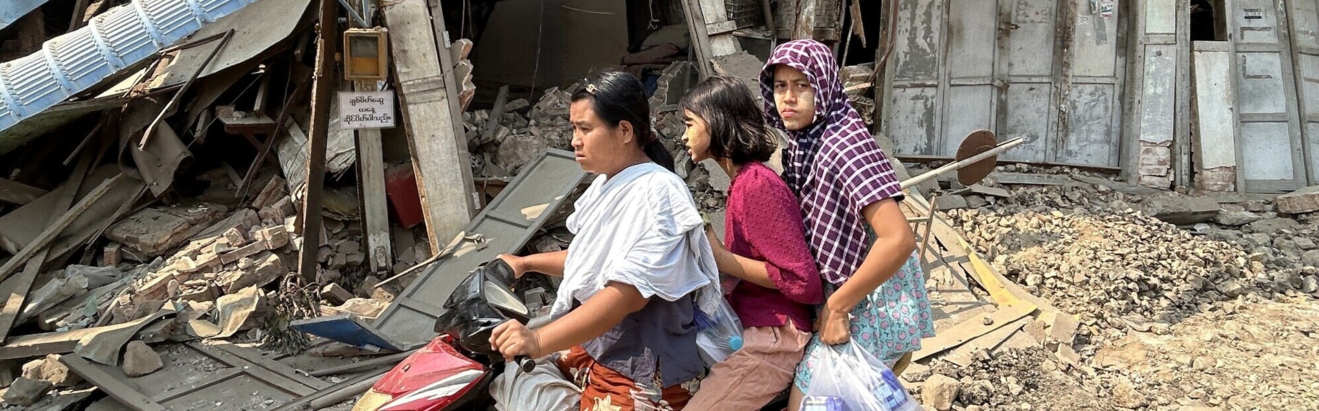 Eine Familie auf einem Moped vor eingestürzten Gebäuden in Myanmar