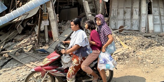 Eine Familie auf einem Moped vor eingestürzten Gebäuden in Myanmar