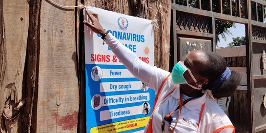 Eine Gesundheitshelferin von World Vision hängt im Südsudan ein Plakat über die Corona-Symptome auf