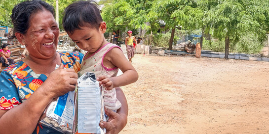Eine Frau mit Kind auf dem Arm erhält von World Vision nach dem Erdbeben in Myanmar Lebensmittelpakete