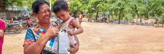 Eine Frau mit Kind auf dem Arm erhält von World Vision nach dem Erdbeben in Myanmar Lebensmittelpakete