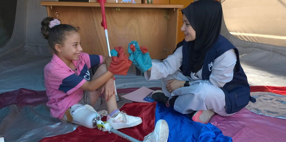 Eine Helferin und ein Kind mit einer Prothese reichen sich die Hände