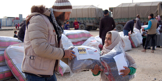 Ein Helfer der Organisation Help – Hilfe zur Selbsthilfe überreicht einem Mädchen eine Hilfslieferung für den Winter