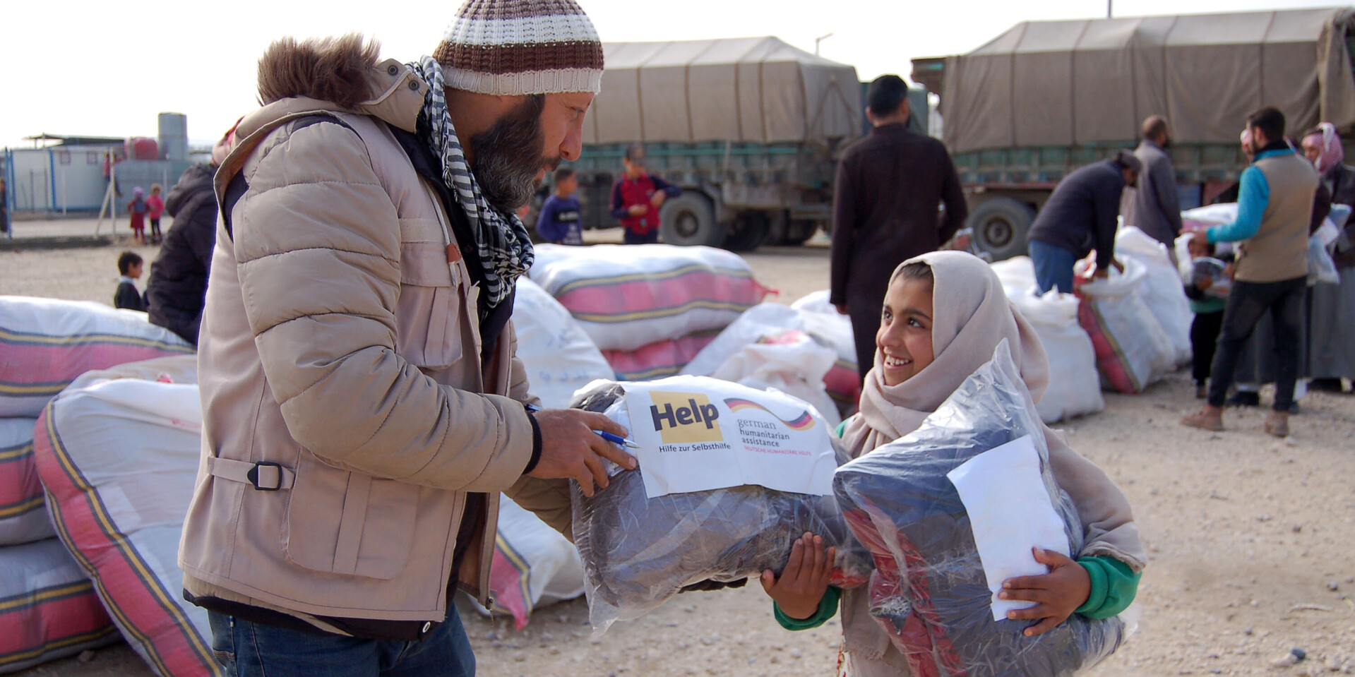 Ein Helfer überreicht einem Mädchen ein Hilfspaket in einem Flüchtlingscamp in Syrien