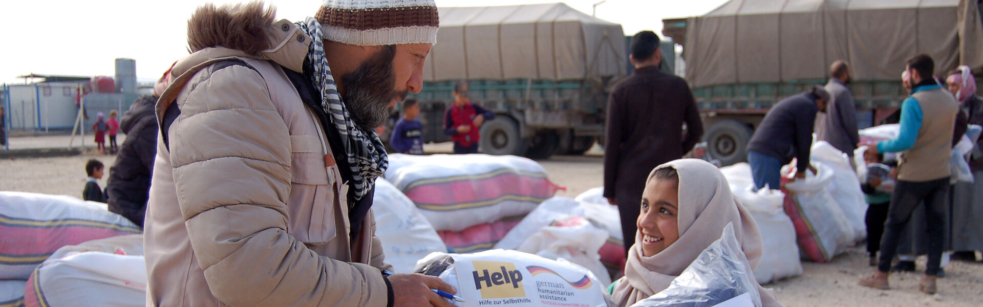 Ein Helfer der Organisation Help – Hilfe zur Selbsthilfe überreicht einem Mädchen eine Hilfslieferung für den Winter