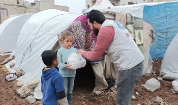 Ein Helfer reicht zwei Kindern in Syrien Hilfsgüter