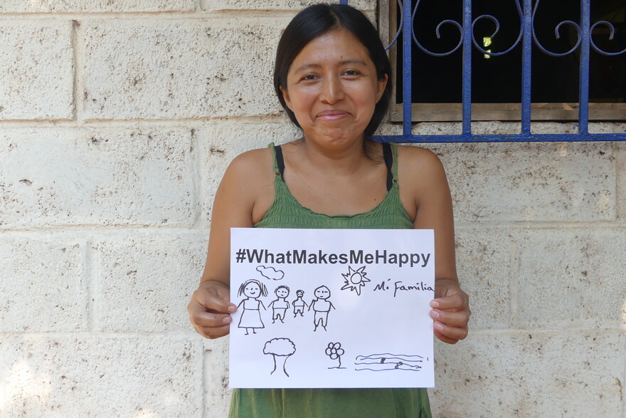 Eine Frau, Noemi, in Guatemala hält ein Schild hoch mit der Aufschrift "#whatmakesmehappy" und dass ihre Familie sie glücklich macht