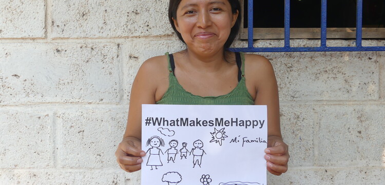Eine Frau, Noemi, in Guatemala hält ein Schild hoch mit der Aufschrift "#whatmakesmehappy" und dass ihre Familie sie glücklich macht