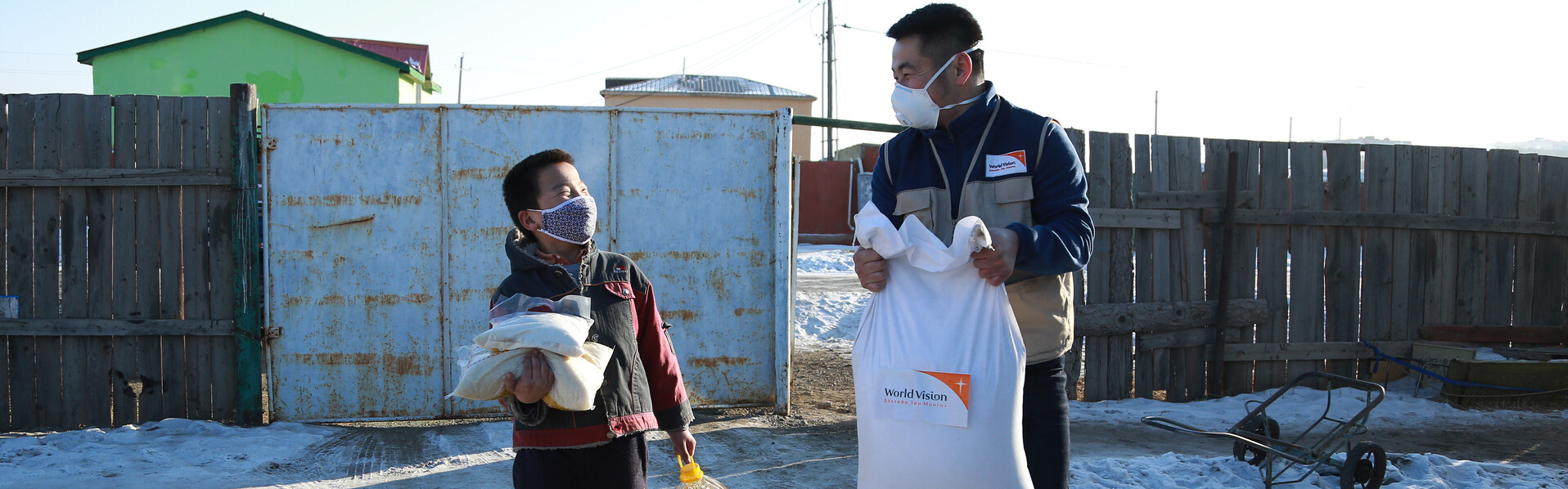 Corona-Nothilfe in der Mongolei: Ein Mitarbeiter von World Vision trägt zusammen mit einem Jungen Lebensmittelsäcke