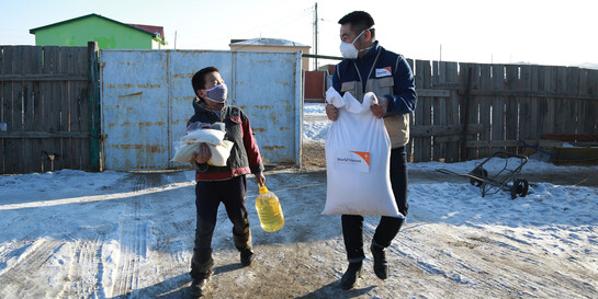 Corona-Nothilfe in der Mongolei: Ein Mitarbeiter von World Vision trägt zusammen mit einem Jungen Lebensmittelsäcke