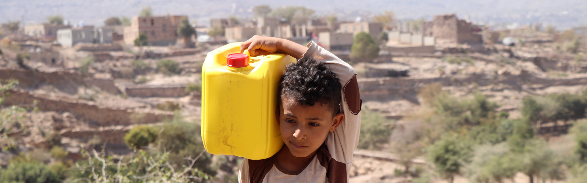 Ein Junge im Jemen trägt einen gelben Wasserkanister auf seinen Schultern 
