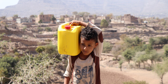 Ein Junge im Jemen trägt einen gelben Wasserkanister auf seinen Schultern 