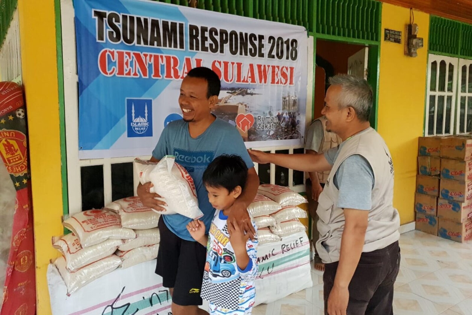 Ein Helfer von Islamic Relief verteilt Hilfsgüter an einen Mann und seinen Sohn auf Sulawesi