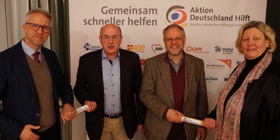 Mit dem Staffelstab übergeben Vorsitzende von Vorstand und Aufsichtsorgan von Aktion Deutschland Hilft ihre Ämter symbolisch an ihre Nachfolge 