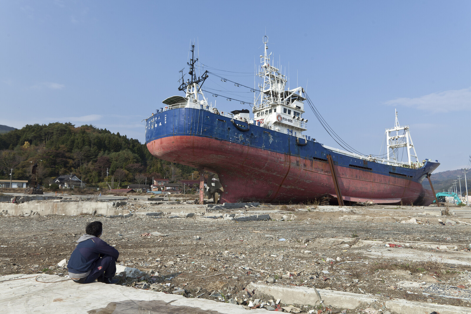 Ein Mann betrachtet ein Frachtschiff, das von einem Tsunami mitgerissen und weit ins Landesinnere getrieben wurde.
