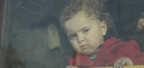 Ein syrisches Kind sitzt hinter einer Glasscheibe