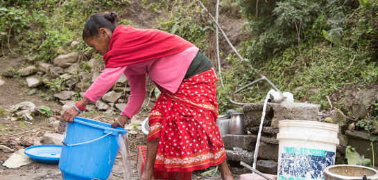 Nach dem schweren Erdbeben in Nepal vor einem Jahr werden Häuser wieder aufgebaut. Eine Frau holt sich sauberes Trinkwasser aus einem Brunnen.