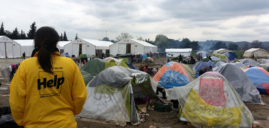 In einem Flüchtlingslager steht eine Frau von Help und beobachtet die Zelte voller Flüchtlinge.