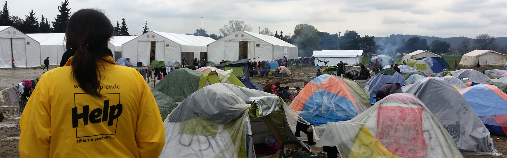 In einem Flüchtlingslager steht eine Frau von Help und beobachtet die Zelte voller Flüchtlinge.