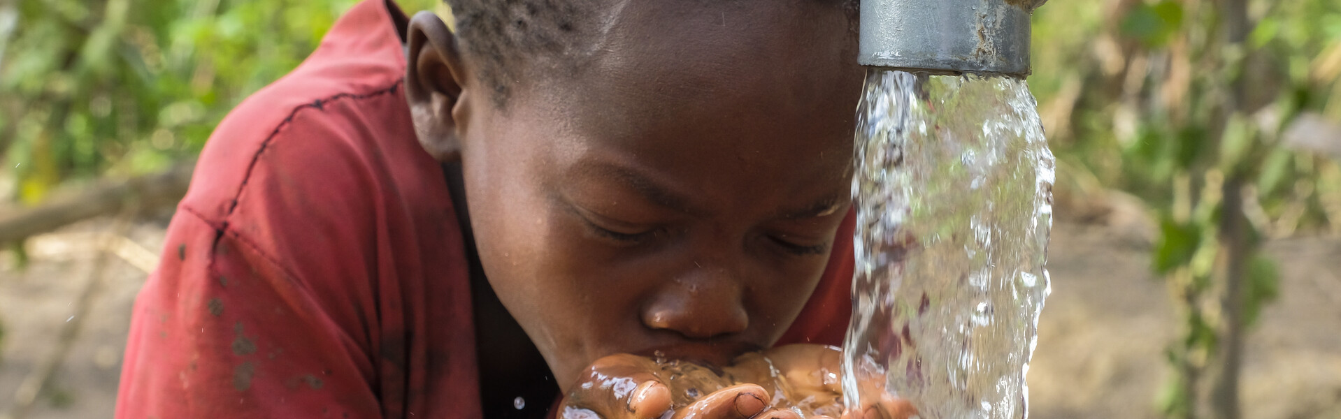 In Uganda trinkt ein Junge sauberes Wasser aus einem Brunnen. 