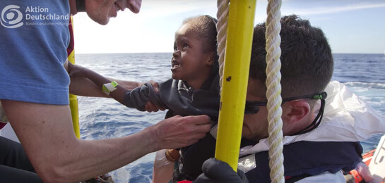 Retter helfen Flüchtlingskind auf das Boot.
