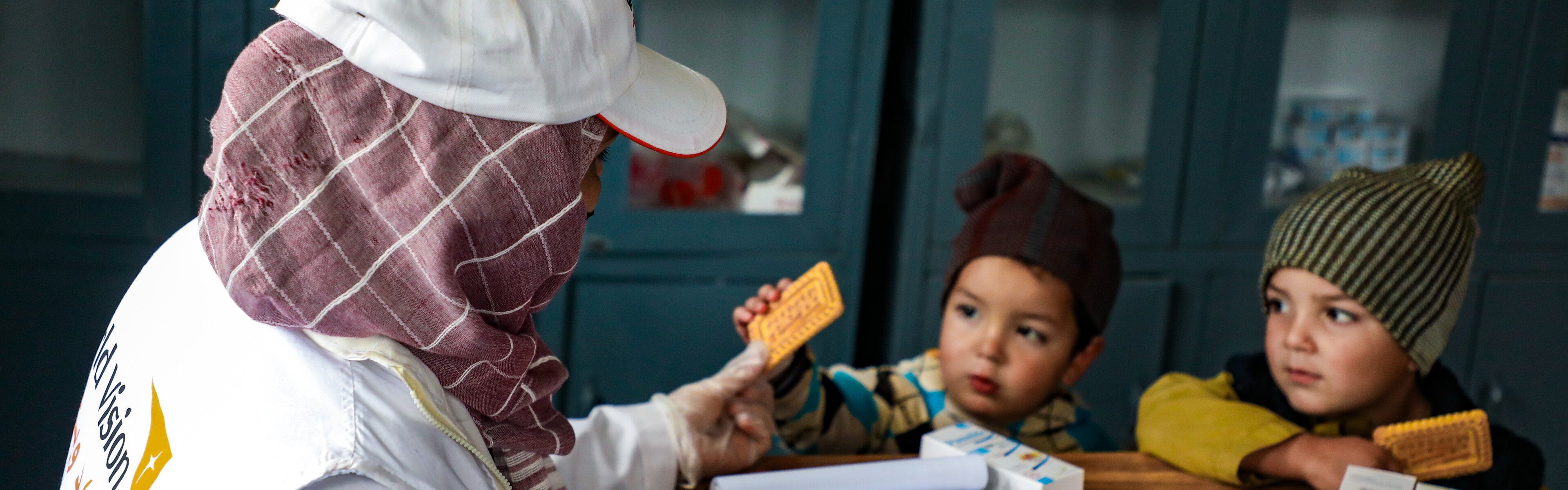 Eine Helferin von World Vision reicht zwei Kindern in Afghanistan einen Keks