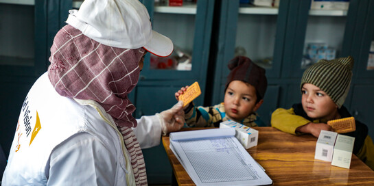 Eine Helferin von World Vision reicht zwei Kindern in Afghanistan einen Keks