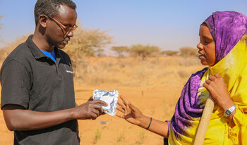 Ein Helfer gibt einer Landwirtin in Somalia dürreresistentes Saatgut